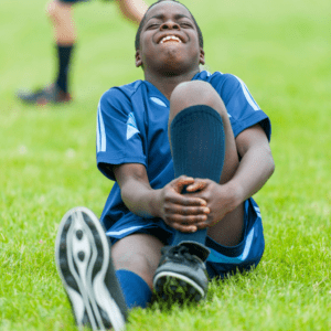 little boy in a soccer uniform and cleats sitting holding leg